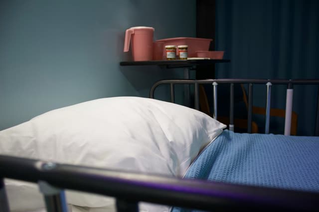Tom hospitalsseng med hvid pude og blåt tæppe samt medicin på sengebord