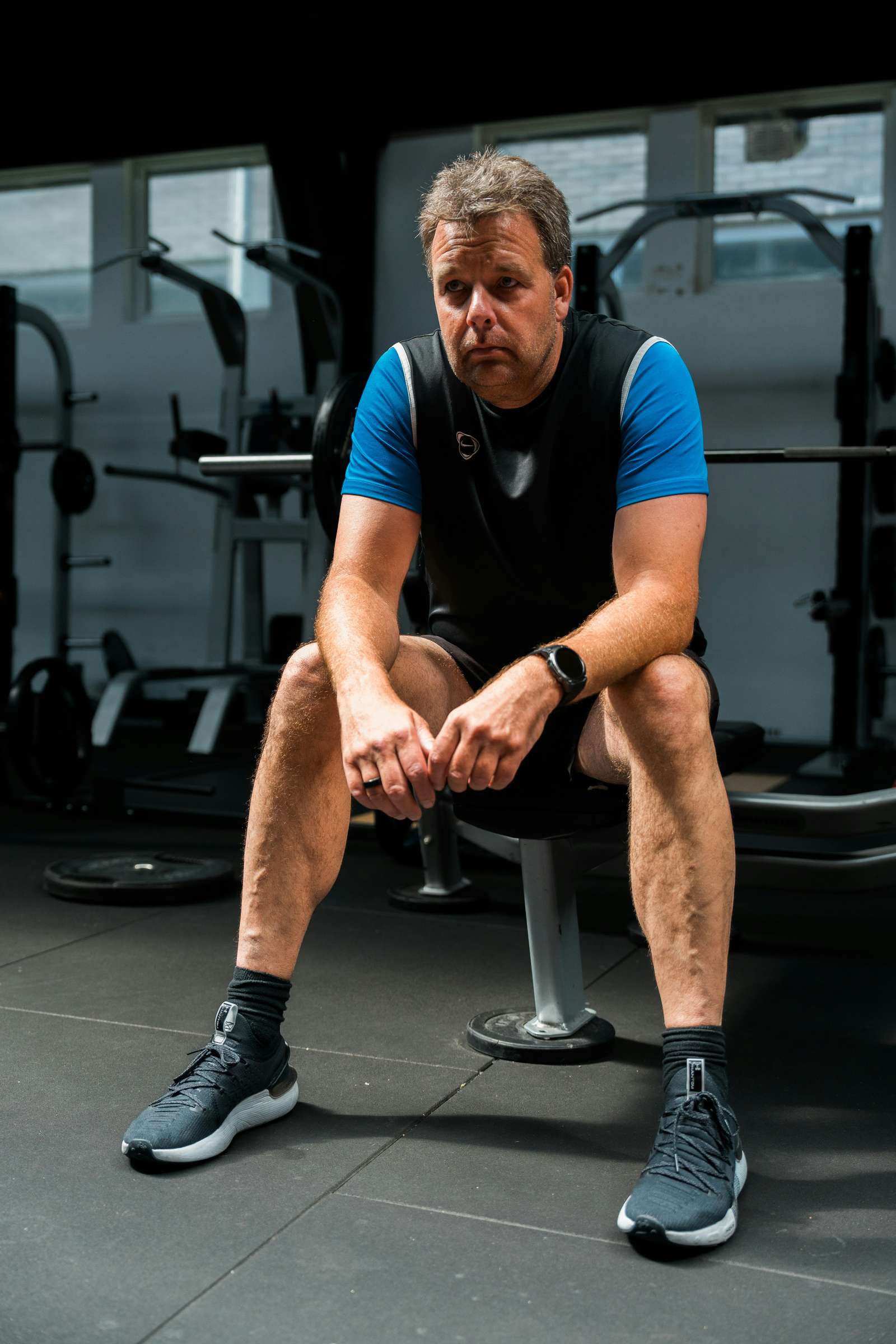 Midaldrende mand i træningstøj sidder eftertænksomt på en bænk i et fitnesscenter