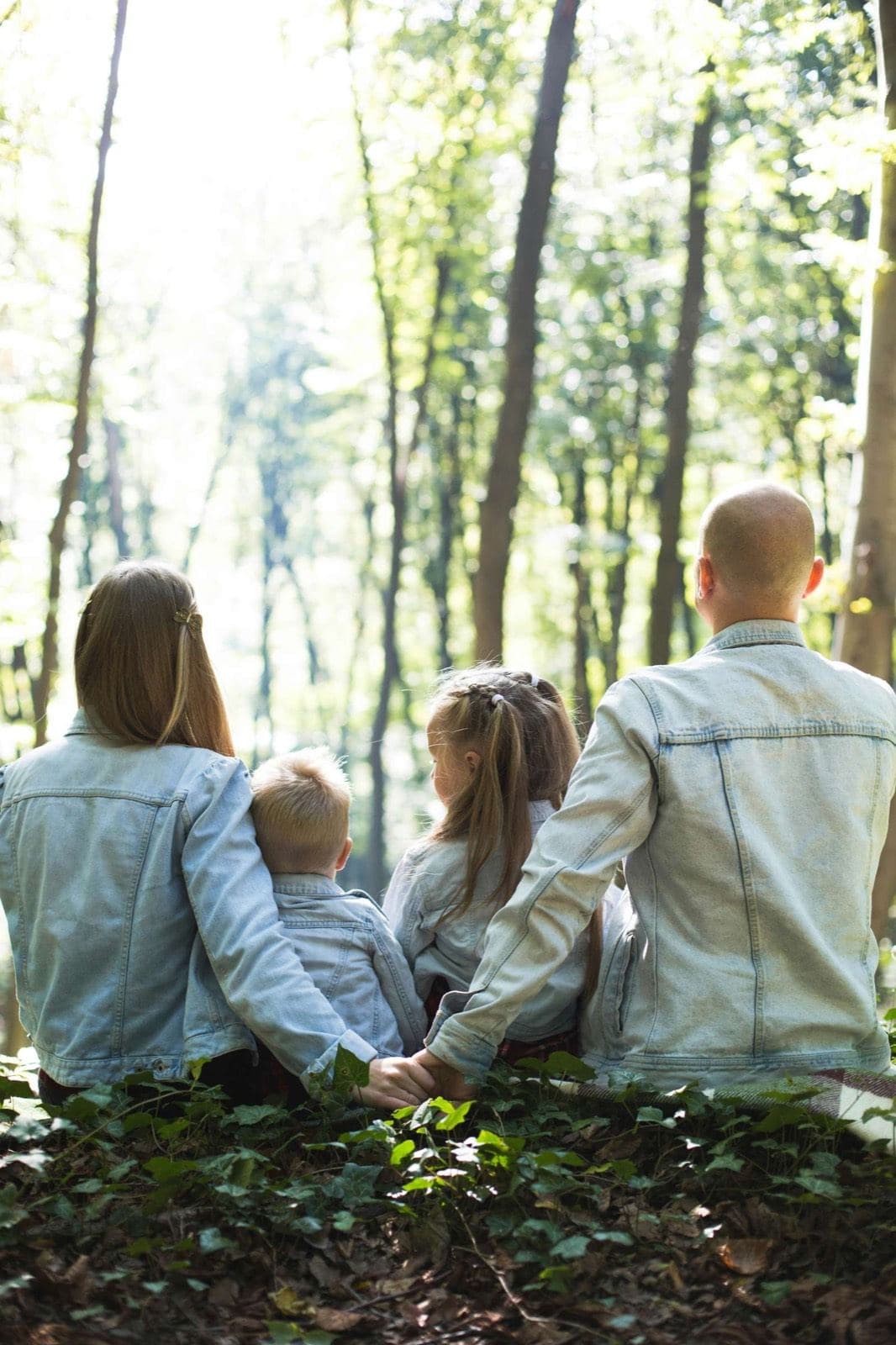 Familie med to børn set bagfra sidder sammen i en grøn skov