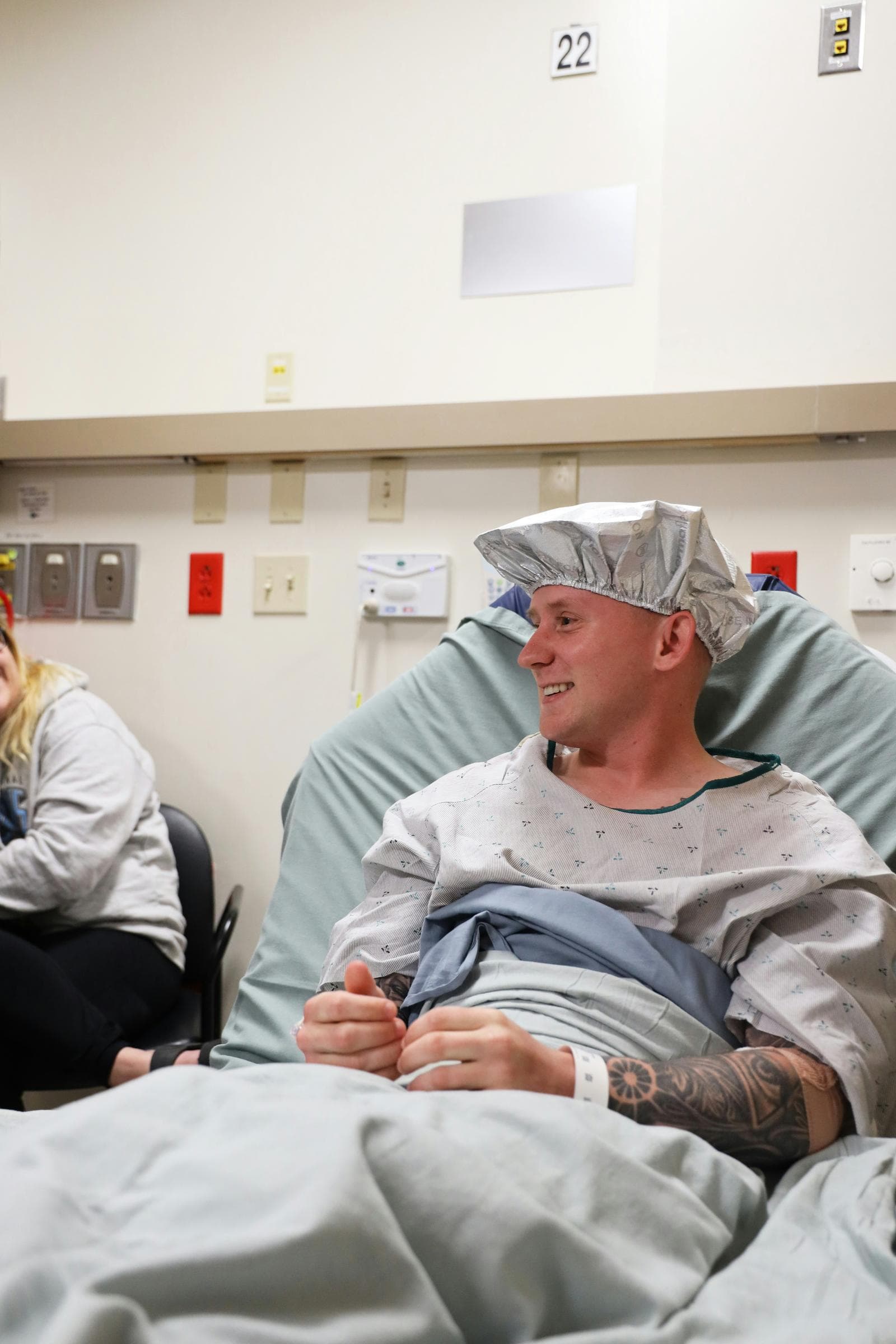 Smilende mand i hospitalskittel og operationshætte sidder i en seng før behandling