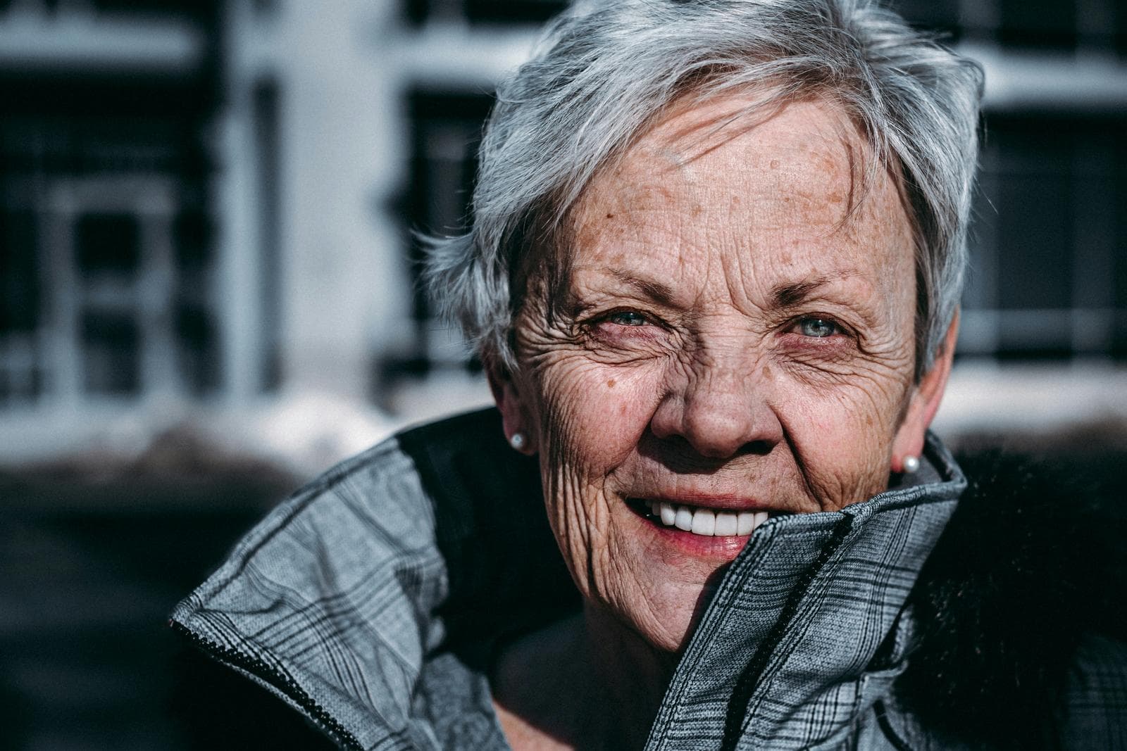 Smilende ældre kvinde med gråt hår og grå jakke udendørs