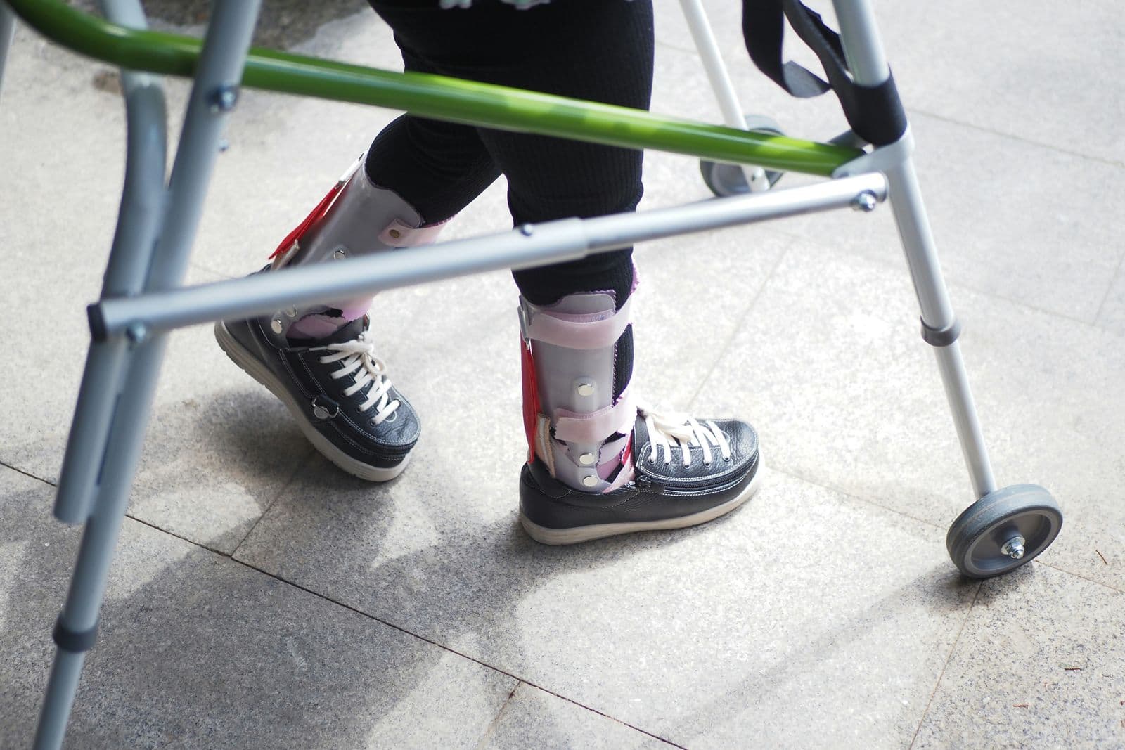 Person med benskinner og ortopædiske sko går med en rollator indendørs